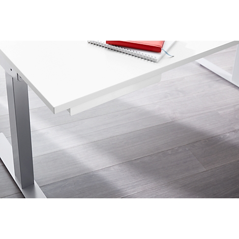 White height-adjustable desk with red notebook. Grey wooden floor.