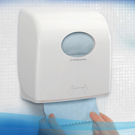 Distributeur d'essuie-mains blanc sur un mur carrelé. En dessous, des mains qui tirent du papier.