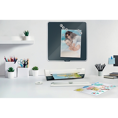 Bureau avec plastifieuse, tableau magnétique avec photo, plantes et stylos.