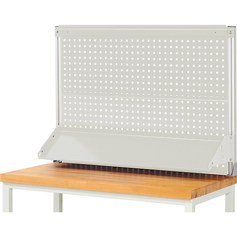 Lichtgrijze pegboard boven een houten werkbank. De muur heeft een plank en wordt ondersteund door een metalen frame.