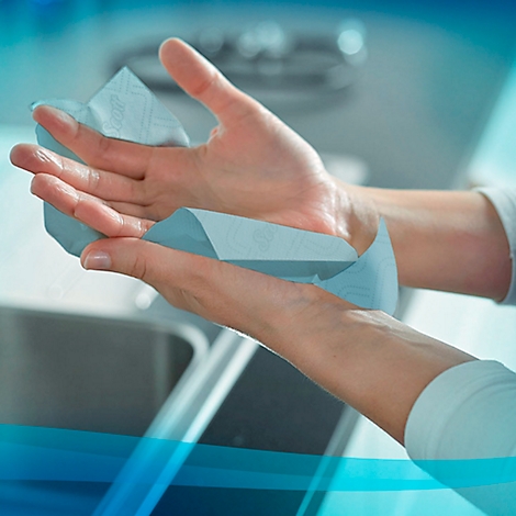 Manos secándose con una toalla de papel azul sobre un lavabo.