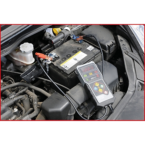 Ein Autobatterietester mit angeschlossenen Klemmen an einer Autobatterie. Der Motorraum ist geöffnet.