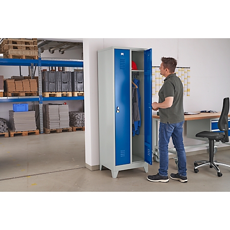 Man opening blue locker. Clothes, helmet and workplace in the background.
