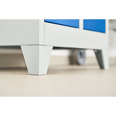 Close-up of the furniture feet of a blue and white cabinet. The feet are trapezoidal and light gray.