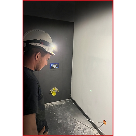 Ein Arbeiter mit Helm und Stirnlampe betrachtet konzentriert eine Baustelle in einem Badezimmer.