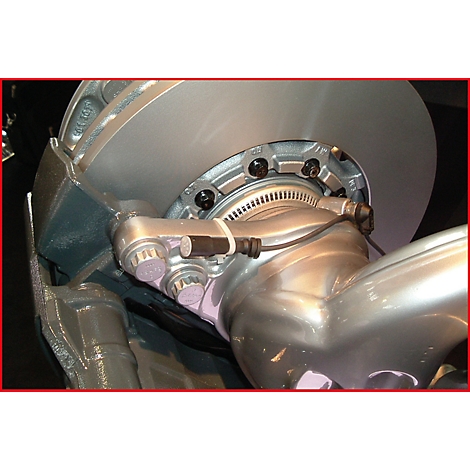 Nahaufnahme einer silberfarbenen Bremsscheibe mit Schrauben und Anbauteilen. Kabel verlaufen entlang der Konstruktion.