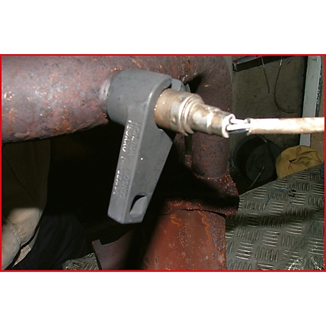 Eine Zange greift einen Sensor an einem verrosteten Auspuffrohr.