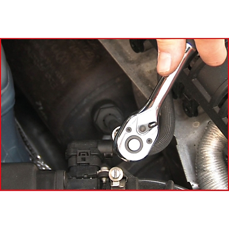 Hand schraubt mit einem Ratschenschlüssel an einem Motorbauteil. Detailaufnahme, Fokus auf Werkzeug.