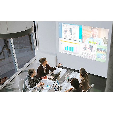 Team meeting with presentation and video. A person is standing and explaining something. Others are sitting at laptops.