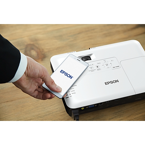 Person holding a smartphone with the EPSON logo in front of white projector. On wooden surface.