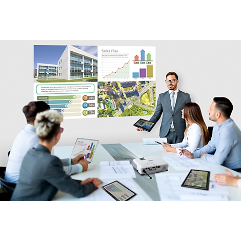 A man presents a presentation with diagrams and photos to a group of colleagues. A projector is on the table.
