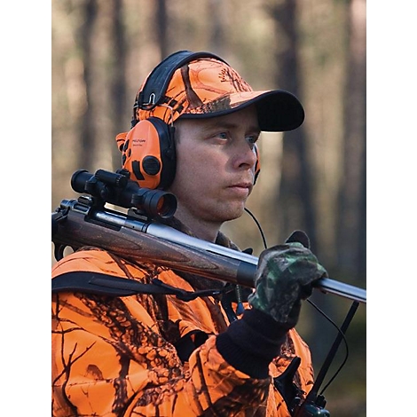 Ein Jäger im Tarnanzug mit Gewehr, Gehörschutz und Mütze im Wald.