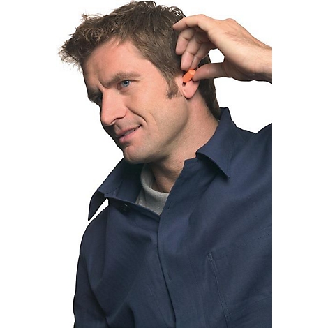 Een man met bruin haar die een oranje oordopje in zijn oor stopt. Hij draagt een blauw overhemd en glimlacht.