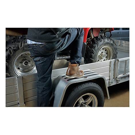 Eine Person steigt auf einen Anhänger. Das rechte Bein steht auf dem Kotflügel, das linke Bein auf der Ladefläche. Im Hintergrund ein rotes ATV.