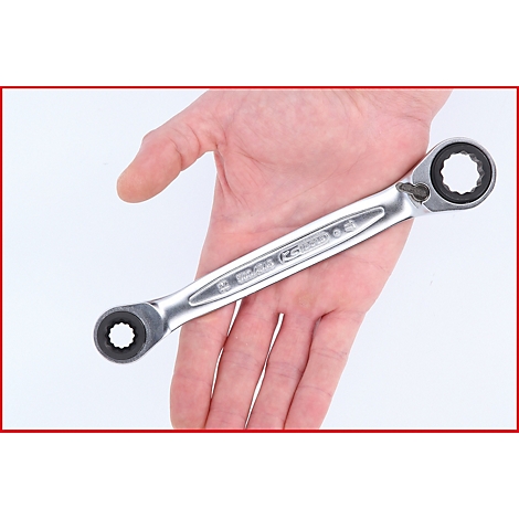 Ein Schraubenschlüssel wird in einer Hand gehalten. Das silberfarbene Werkzeug hat an beiden Enden einen runden Kopf mit gezahnten Öffnungen.