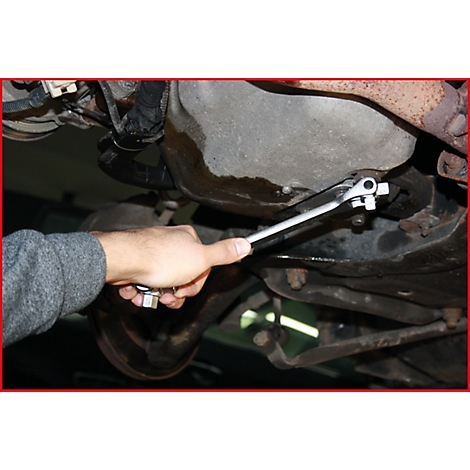 Ein Mann arbeitet unter einem Auto und benutzt einen Schraubenschlüssel, um eine Schraube zu lösen.