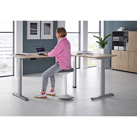 Een vrouw zit aan een in hoogte verstelbaar bureau en werkt op een laptop.