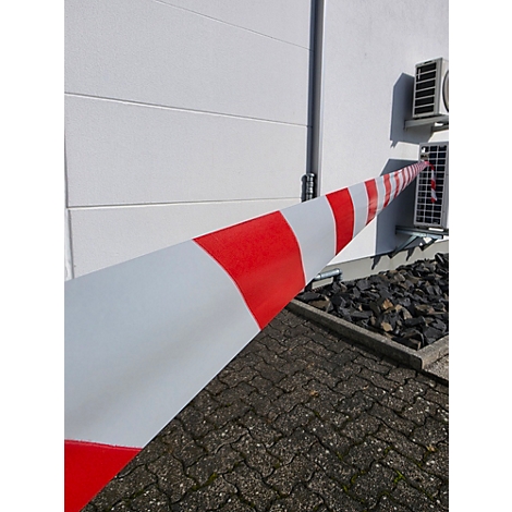 Rot-weißes Absperrband verläuft diagonal durch das Bild zu einem Klimagerät an einer weißen Hauswand.