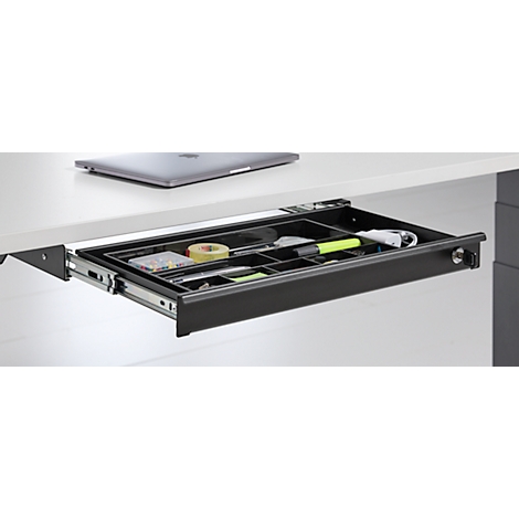 Uitgetrokken lade onder een bureau met pennen, tape, markeerstift en notities. Een laptop staat erboven.