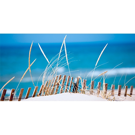 Dune landscape with beach grass and wooden fence against blue sea.