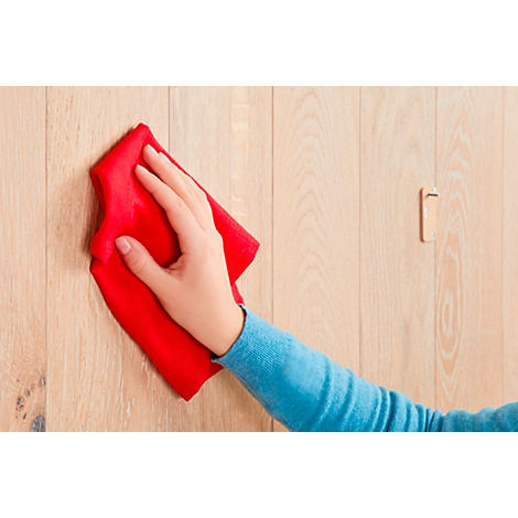 A hand wiping a wooden wall with a red cloth. A door handle can be seen in the background.