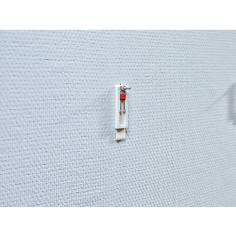 A white picture hook with red detail on a white wall.