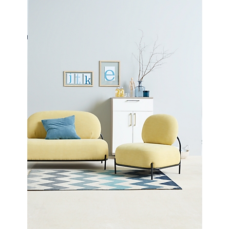 Yellow sofa and armchair with black metal frames on a rug. In the background a cabinet with decoration and pictures.