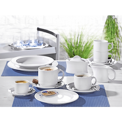 Coffee set with cups, saucers, milk jug and sugar bowl on a table. Plants can be seen in the background.