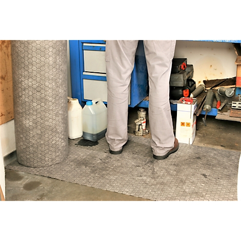 Una persona con pantalones color beige y zapatos marrones está de pie en un taller. Hay un objeto cilíndrico gris y armarios azules.