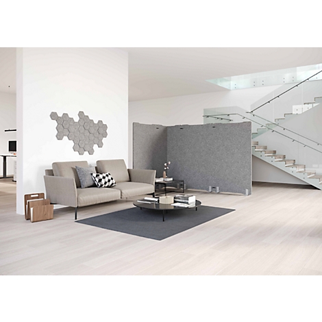 Ein helles Wohnzimmer mit Sofa, Couchtisch, Raumteilern und Treppe. An der Wand sind sechseckige graue Elemente angebracht.