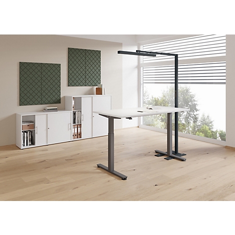 Ein höhenverstellbarer Schreibtisch im Büro. Ein Fenster und Schränke sind im Hintergrund zu sehen.