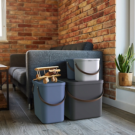 Three trash cans in different colors, next to a toy airplane and a potted plant.