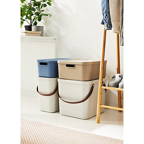 Stacked beige and blue storage boxes next to a clothes stand and plant.