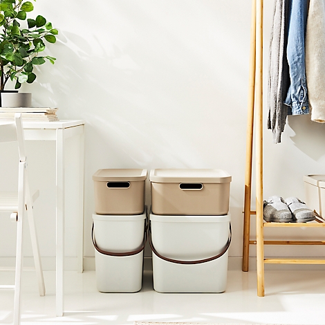 Two beige lidded boxes sit atop two white buckets. To the right, a clothes rack with clothes.