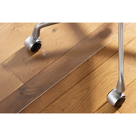 Primer plano de ruedas de silla sobre un suelo de madera. Las ruedas son de metal y tienen ruedas negras.