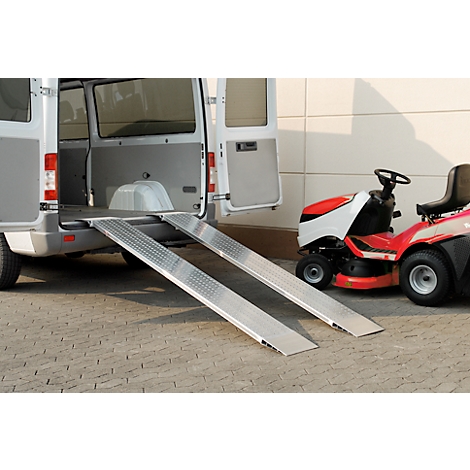A white van tailgate with two aluminium ramps, next to it a red lawn tractor.