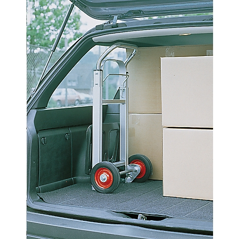 A silver hand truck stands in a car. Cardboard boxes are stacked next to it.