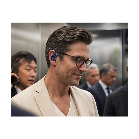 Ein Mann mit Brille trägt einen blauen Ohrhörer in einer belebten Umgebung.
