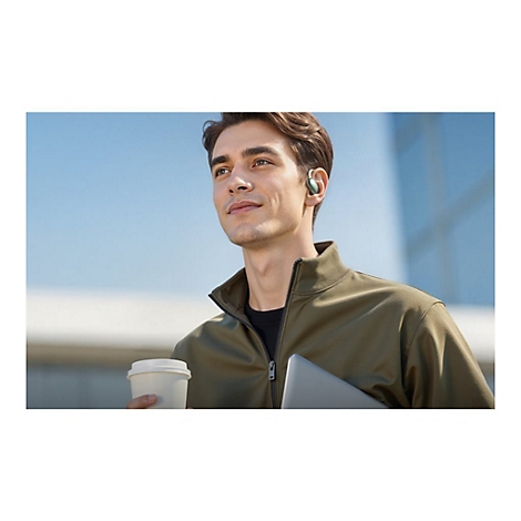 Ein junger Mann mit offenem Blick trägt einen grünen Ohrhörer und hält einen Kaffeebecher in der Hand.