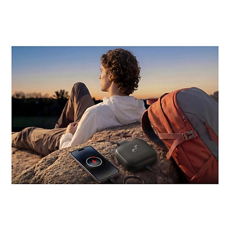 Ein Mann sitzt bei Sonnenuntergang auf einem Felsen, während ein Lautsprecher sein Smartphone auflädt.