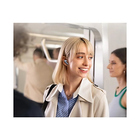 Eine lächelnde junge Frau mit blonden Haaren trägt kabellose In-Ear-Kopfhörer in einem Zug.