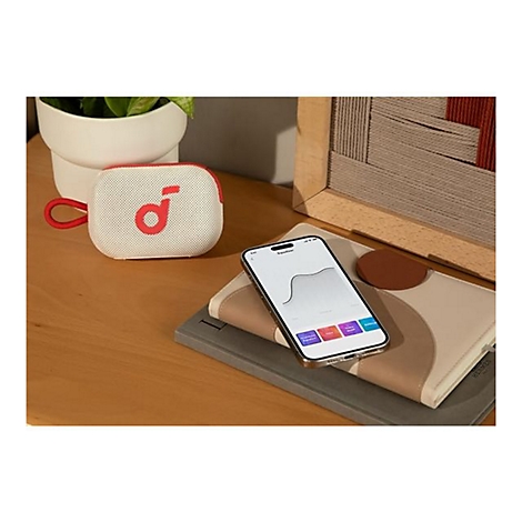 Ein weißer, kompakter Bluetooth-Lautsprecher neben einem Smartphone, das eine Equalizer-App anzeigt, auf einem Holztisch.
