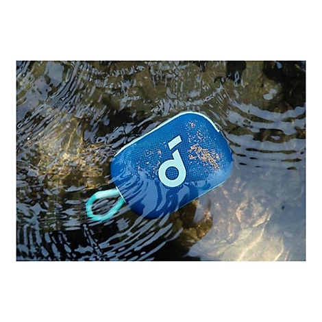 Ein blauer, wasserfester Lautsprecher mit Trageschlaufe schwimmt halb untergetaucht in einem fließenden Bach.