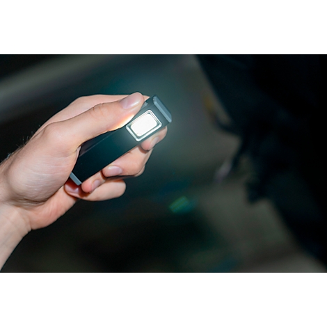 Een hand die een aangestoken, zwarte LED-zaklamp vasthoudt. De heldere lichtbundel schijnt naar voren.
