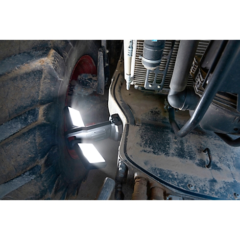 Nahaufnahme eines Traktorreifens und Motorteilen. Staub bedeckt die Metalloberfläche, Sonnenlicht fällt durch eine Öffnung.
