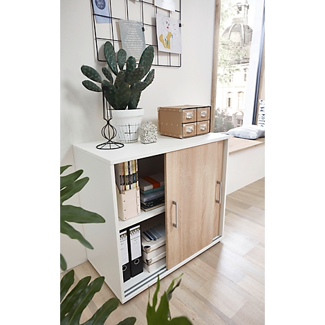 Weißer Schrank mit Holzschiebetür, darauf Kakteen, Deko und Schubladen. Im Regal Bücher, Ordner und Deko.