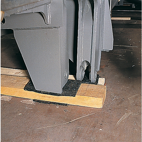 Gray machine part stands on a wooden block with a black base. Brown floor.