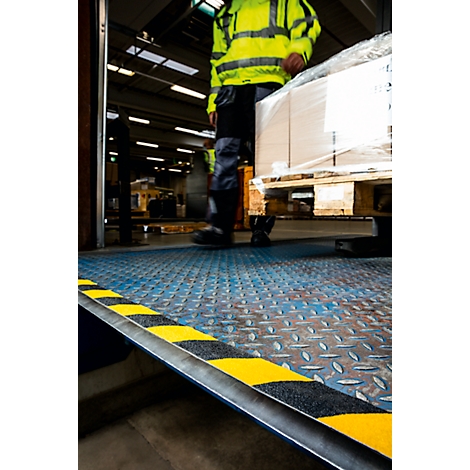 Worker transporting goods on a pallet. Yellow and black markings on a ramp.