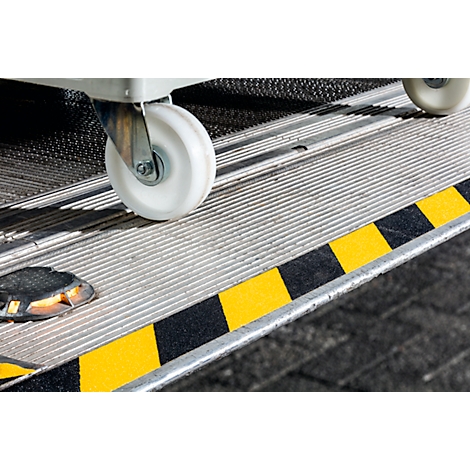 Close-up of a loading ramp with warning markings, wheelchair wheel, and a lighted obstacle.