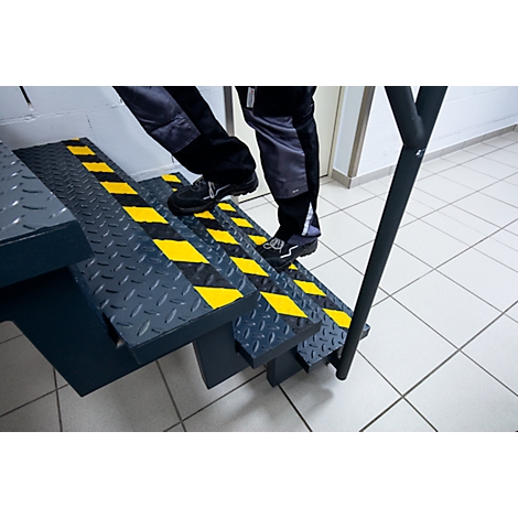 Person climbing stairs with yellow and black markings. Metal railing.